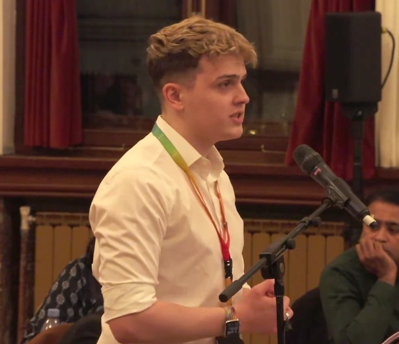 Photo of Nate proposing the motion. He is at a microphone wearing a white shirt.